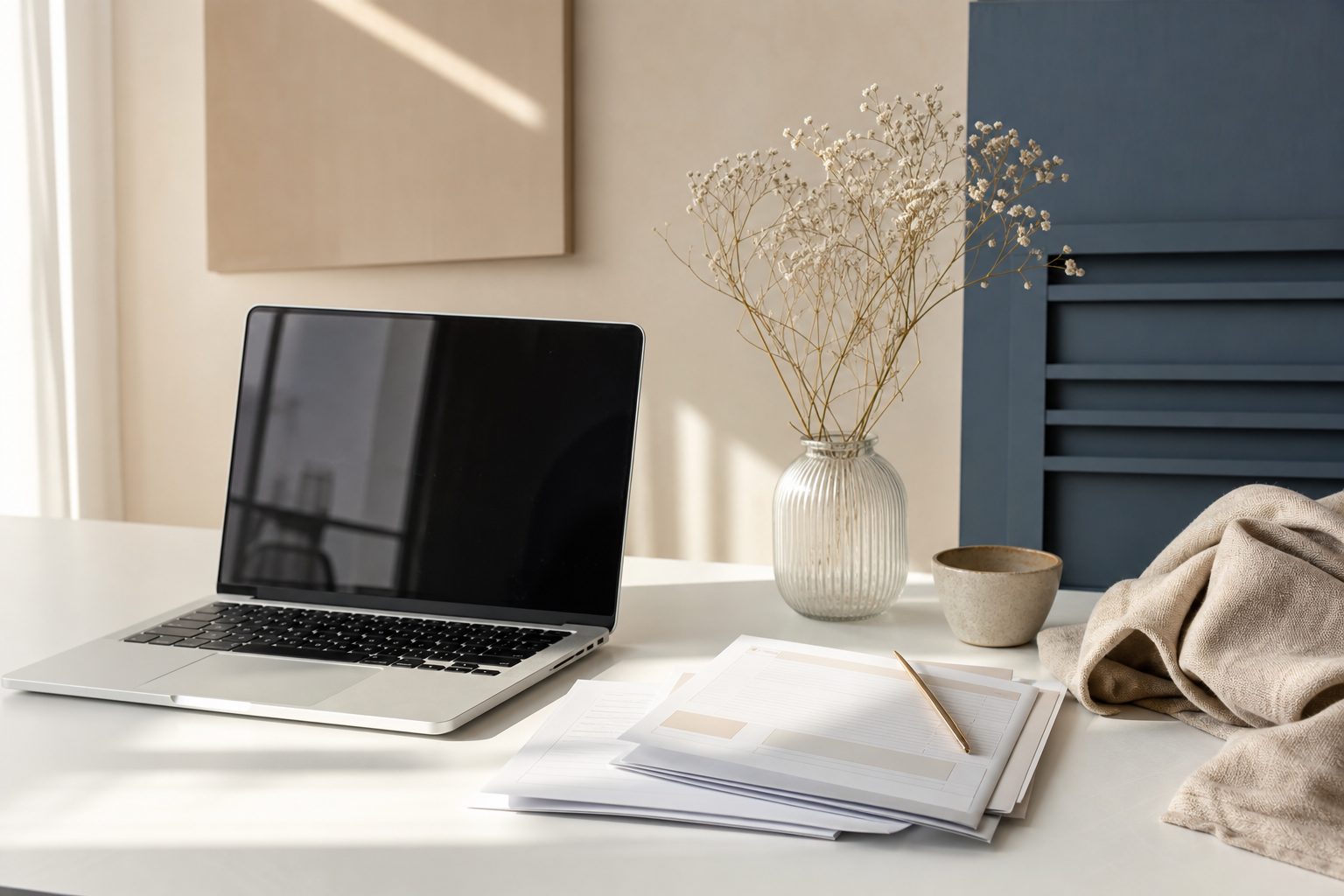 Open laptop and paper forms on a white desk in a sunlit studio office