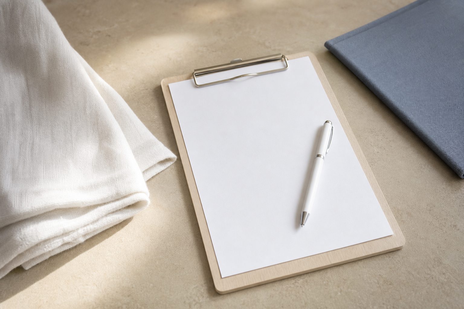Clipboard with a blank intake form and pen on a warm desk beside folded linen